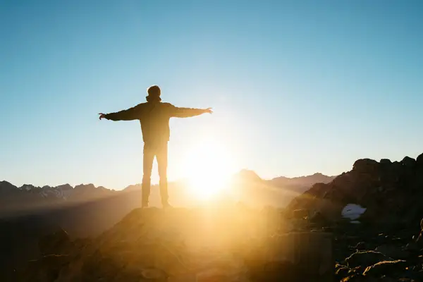 Person standing with arms outstretched towards the sun, representing hope and mental wellness